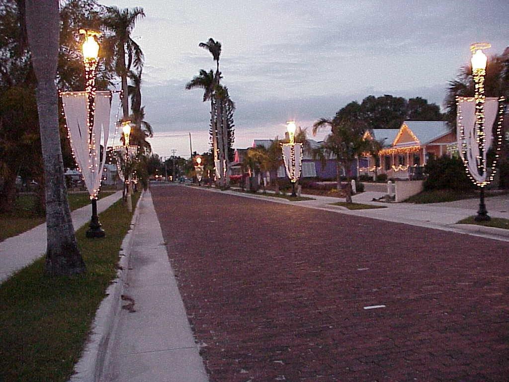 Brick paved street. Light poles decorated with holiday lights. Homes in background.