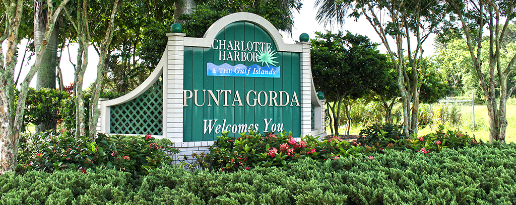 Photo of Punta Gorda Welcome Sign sent in landscaped area of trees and shrubs. 